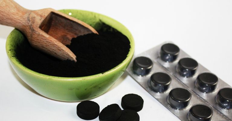 Black activated charcoal tablets and powder in a bowl on white background